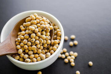 Soy bean seed organic on wooden spoon with white cup and black wooden background. flat lay with free space. raw vegetarian protein  food diet for good health concept.
