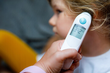 Mother takes temperature for her little preschool daughter, sick child with infrared in ear...