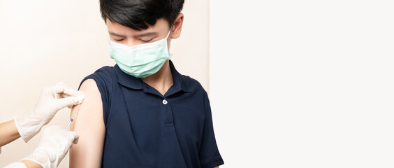 COVID 19 Vaccination for kids and teenager concept. Smart Asian teen boy with medical face mask looking at nurse's hand with syringe, receiving vaccine injection at hospital. Herd immunity, safe, prot