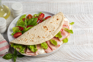Piadina romagnola, traditional italian flatbread with ham, soft cheese  and lettuce. Fresh summer lunch. On a white wooden table.