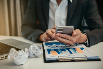 Fototapeta premium Business documents on office desk with smart phone and graph business diagram and man working at office.