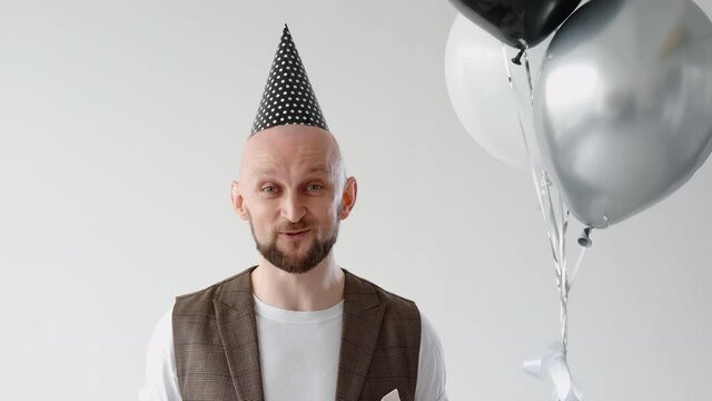 Birthday greeting. Festive congratulation. Special occasion video message speech. Excited smiling happy man in party hat with balloons saying nice words blowing horn throwing confetti.