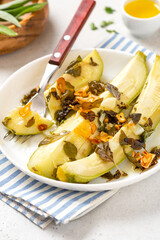 Stewed zucchini with herbs and garlic in a white plate on a gray concrete background. Summer recipes, vegan food, diet.