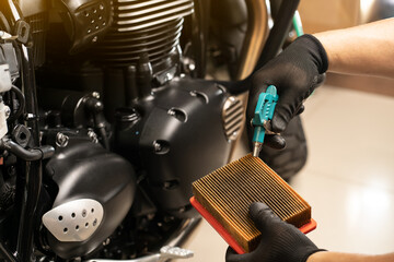 mechanic holding dirty Engine Air Filter over motorcycle and cleaning Filter with air blow gun...