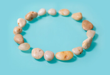 A circle of sea pebbles close-up on a turquoise glossy background.