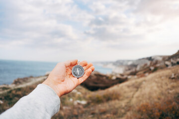 Man with a compass orientates himself in a mountainous area, point of view.
