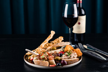 Italian antipasti wine snacks set. Brushettas, cheese variety, Mediterranean olives and wine in glasses over black grunge background