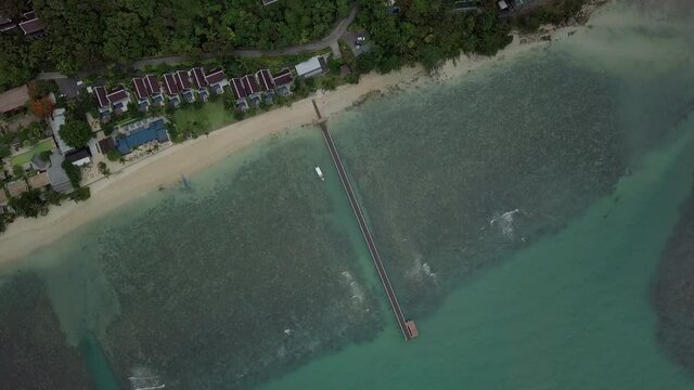 Birds view angle of long pier in tropical waters with beach and house roofs at Koh Samui island in Thailand - drone rotaing
