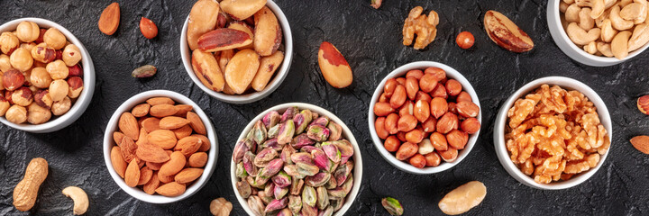 Nuts overhead flat lay panorama with pistachios, almonts, peanuts and many other nuts on a black slate background