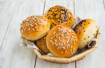 Homemade hamburger buns with sprinkles in a wicker basket on a light wooden background.