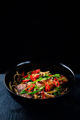 Rice noodles with vegetable stir fry on the ceramic plate on dark background