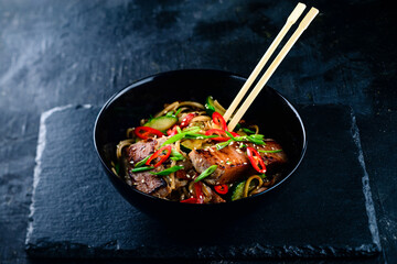delicious noodles with tuna and vegetables on a dark stone background