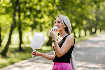 A young woman with cotton candy walks along an alley in the park