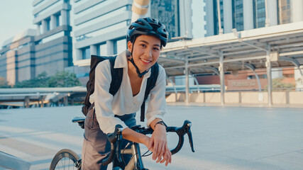 Asian businesswoman go to work at office stand and smiling wear backpack look at camera with bicycle on street around building on a city. Bike commuting, Commute on bike, Business commuter concept. - obrazy, fototapety, plakaty