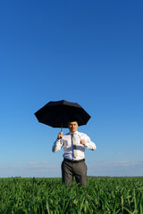 businessman poses with umbrella in a field, green grass and blue sky as background
