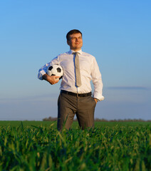 Naklejka na ściany i meble businessman poses with soccer ball in a green grass field - freelance, sport and business concept