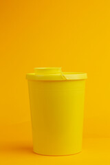 Front view of container with round cap on seamless yellow background for the disposal of used injector needles with drug residue. Studio medical equipment still life concept.
