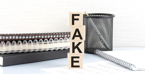 FAKE text on the wooden block with notebooks on white background