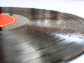 Part of a phonograph disc record with spiral grooves and a red label. Close-up, blur effect, selective focus on center of image