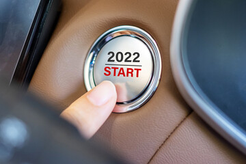 Finger press a car ignition button with 2022 START text inside modern electric automobile. New Year...
