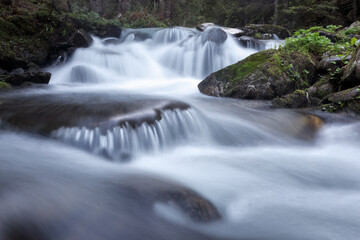 Mountain waterfall flows among green forest and runs down the beautiful gray stones. Amazing summertime wallpaper background.