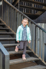 Little caucasian blonde girl in a fashionable outerwear stands on staircase