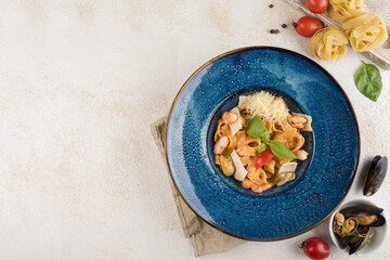 Italian pasta with seafood and fresh basil on a blue plate with a napkin on a light background.
