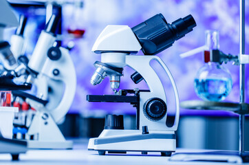 Microscope in and laboratory with chemical test tube equipment in lab blue lights, science and experiment concept