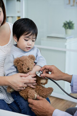 Doctor listening to heart of of teddy bear in hands of little kid to calm him before examination