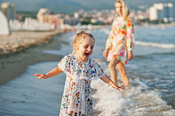 Naklejka premium Mother and beautiful daughter having fun on the beach. Portrait of happy woman with cute little girl on vacation.