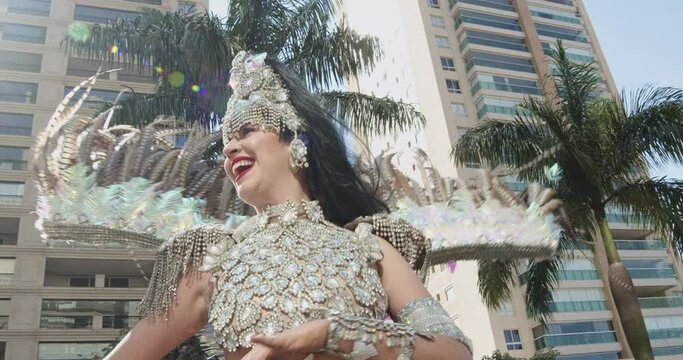 Beautiful Brazilian woman wearing colorful Carnival costume dancing and smiling during Carnaval street parade in city. Cinematic 4K.