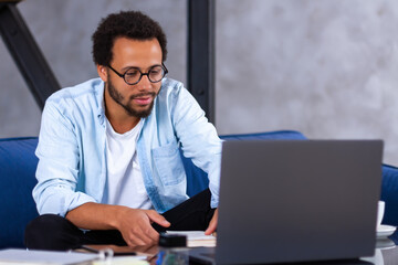 An African-American smiling businessman using laptop computer app for communication with diverse team on distance. Black man freelancer is talking with colleagues online. Video meeting concept.