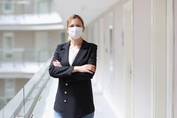 Young woman in suit and protective medical mask standing in corridor of hotel