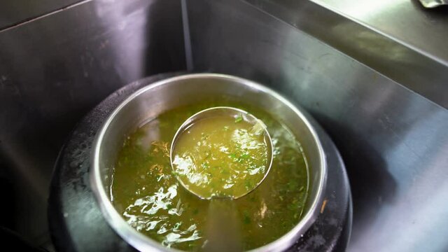 Close-up on a large ladle, hot and delicious soup is being collected from a large saucepan that stands on the line of food distribution in the buffet.
