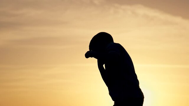 Silhouette of kid in park. Boy is engaged in boxing with shadow in park. Kid boxing. Silhouette of child at sunset in park. Happy boy goes in for sports boxing with shadow. Happy child at sunset