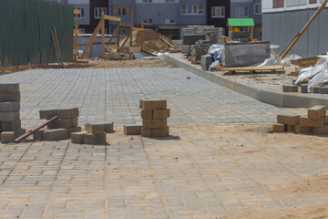 Laying paving slabs on the sidewalk in the city near a new house under construction