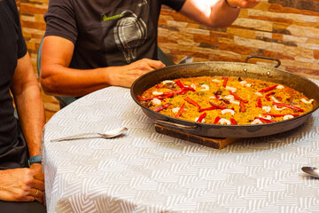 Gathering of friends eating paella. A family making paella. Spanish traditional cuisine: yellow rice with shrimps, chicken and red pepper.