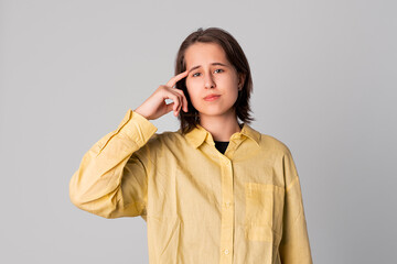 Studio portrait of a thinking pose girl touching herself head by index finger, dressing in stylish yellow shirt. Concept of thinking