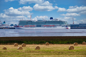 View over a meadow with bales of straw to the port of Bremerhaven / Germany where a cruise ship is anchored 