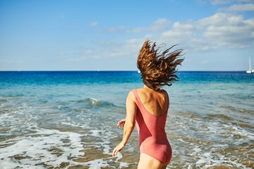Naklejka premium Mature woman having fun jumping on the beach during summer vacation - Focus on female back
