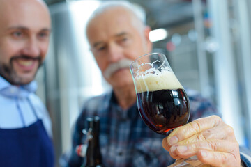 men in brewery tilting glass to examine ale