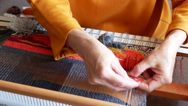 Weaver is tying knots to create a cut pile carpet effect. Making coloured and textured tapestry. Hands of artisan at work. Tapestry weaving