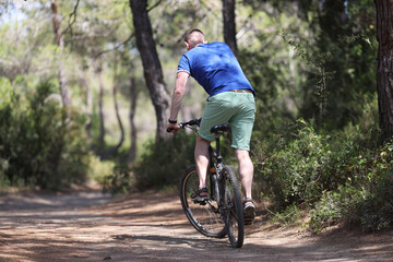 Fototapeta na wymiar Young man riding bicycle along path of park back view