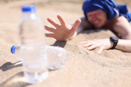 Dehydrated Man Crawling On Sand For Bottle Of Drinking Water Closeup