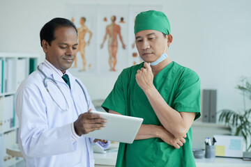 Pensive surgeon looking at patients x-ray on tablet computer in hands of chief physician