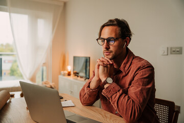 Caucasian male student listening to lectures online with earphones studying at home