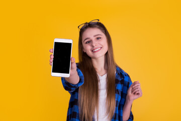 Beautiful girl showing phone  in a blue shirt on a yellow background
