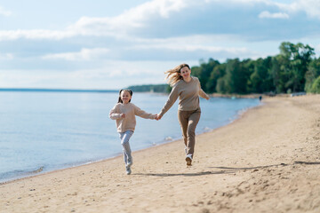 A young woman and a girl running at the beach hand by hand 