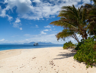 Paradise place to relax - palm trees, sandy beach, white yacht, azure ocean and huge blue sky.