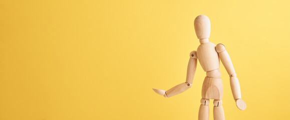 Wooden doll with gesture on yellow background. Mannequin shows gesture. Figure of wooden human with copy space